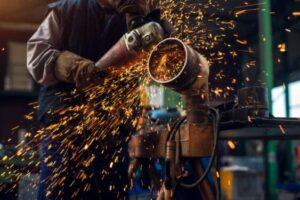 African Development Bank partner’s with African Guarantee Fund to provide loans to women entrepreneurs side close up view professional focused hardworking man uniform working metal tube sculpture with electric grinder while sparks flying industrial fabric workshop 232070 6617