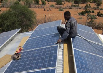 A greenn energy worker lays down solar panels on a rural house roof. Photo/Greenlight Planet