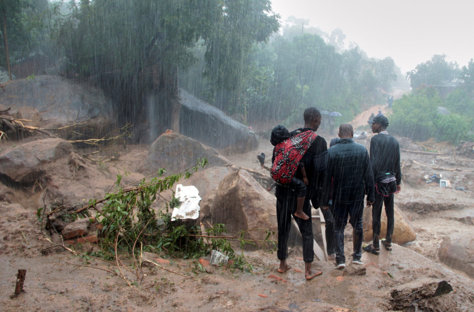 Cyclone Freddy: Malawi struggling to recover, food prices soar. In the picture a man carrying a baby on his back stands stranded with several others as rains continue to pour. Photo/TheNewHumaniterian