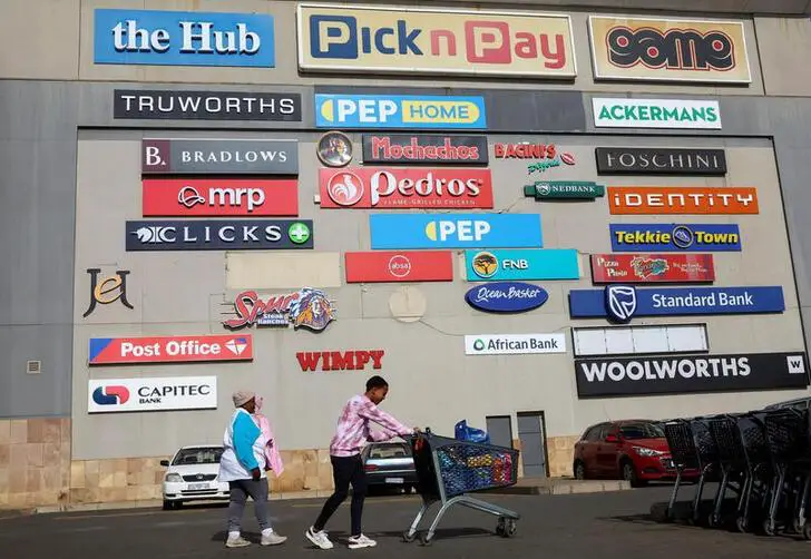 A shopper pushes a trolley as logos of shops are seen on a wall at a shopping mall in Lenasia, south of Johannesburg, South Africa, June 28, 2022. www.theexchange.africa